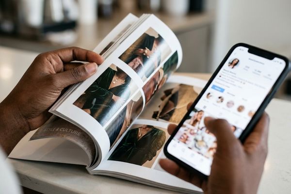 Close-up of Black hands holding an unbranded magazine and a smartphone displaying Media Beauty Standards.